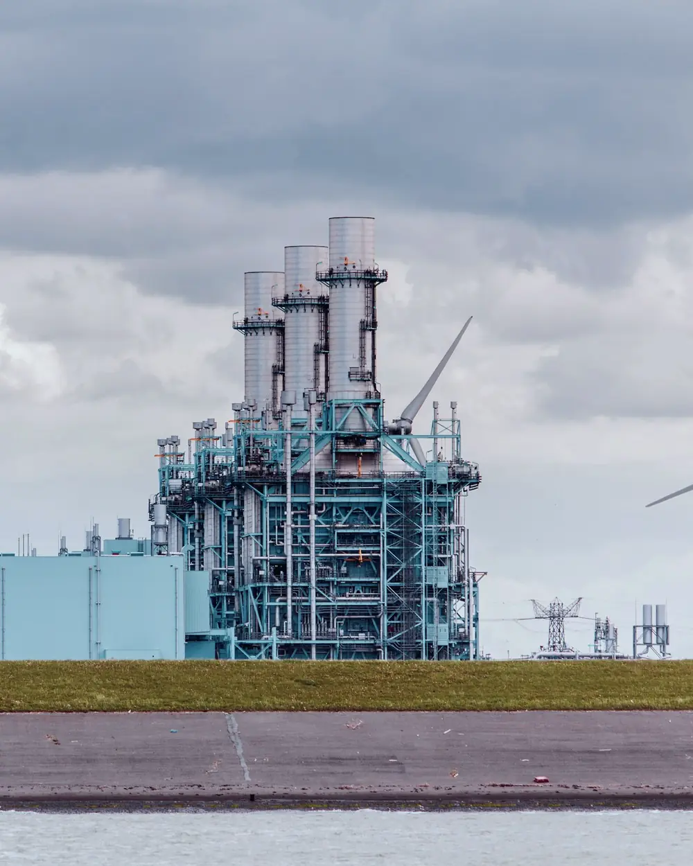A gas-fired power plant beside wind turbines under a pale sky